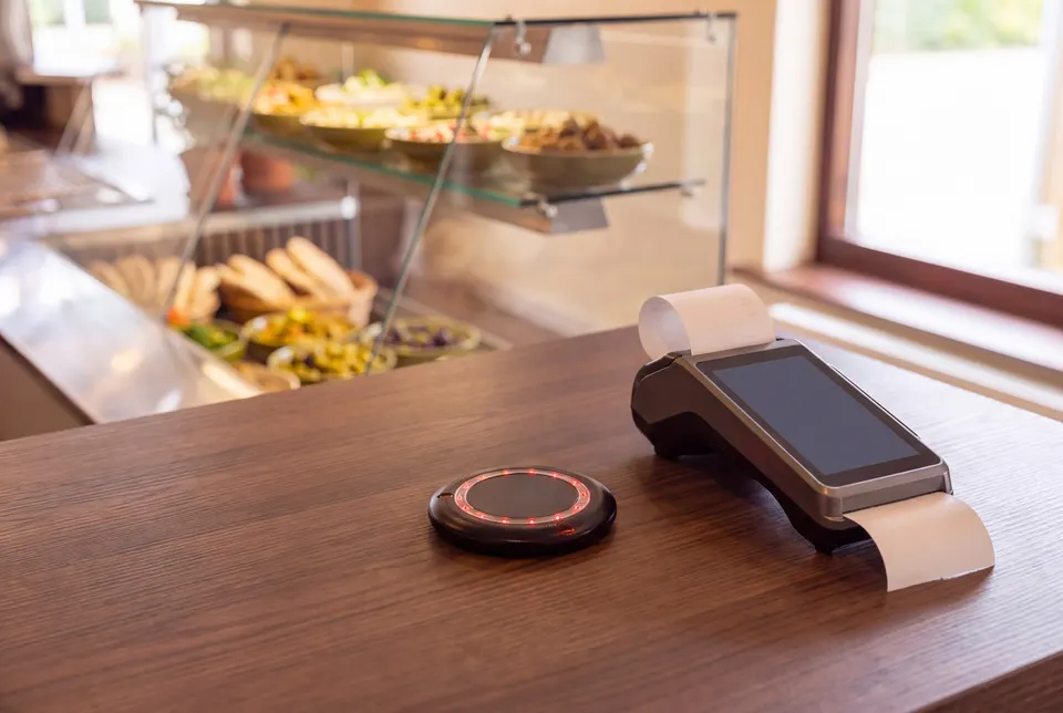Schwarzer Restaurant-Pager mit rotem Leuchtring auf der Theke neben dem Kartenterminal (Symbolbild auf Basis einer Aufnahme des Lokals)